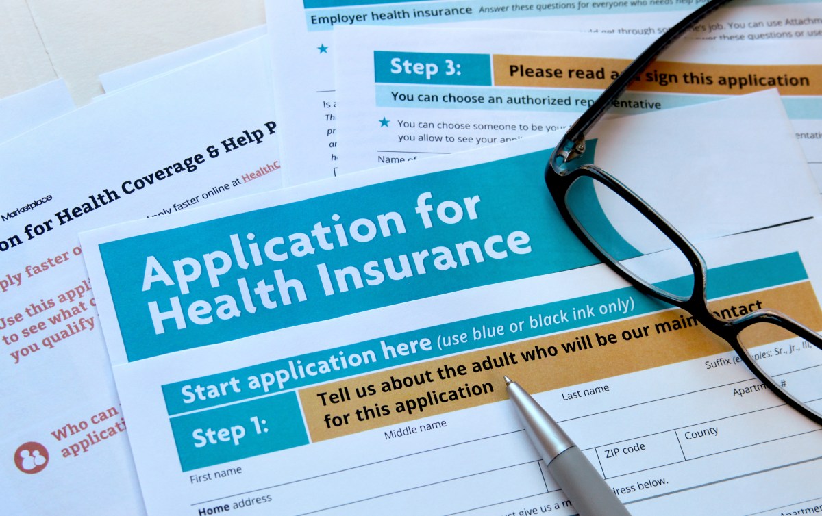 A small pile of papers for an application for health insurance with a pair of glasses and a pen on top.