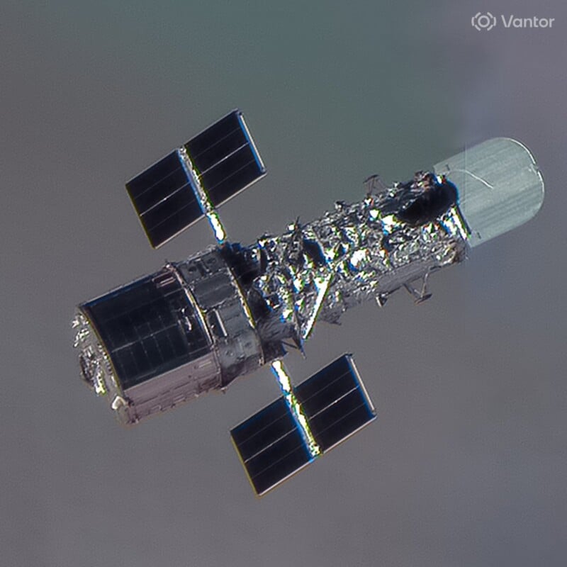 A satellite with four solar panels and a cylindrical body orbits in space against a blurred backdrop; its metallic structure and details are clearly visible.