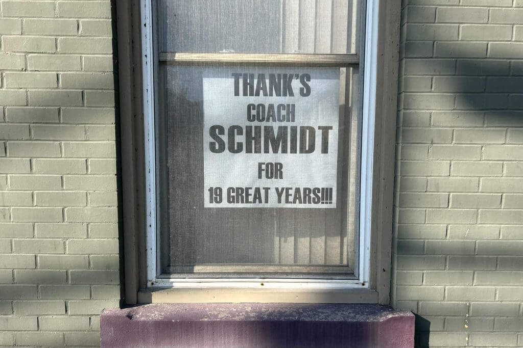 A sign hangs in a window saying "Thanks Coach Schmidt for 19 great years!!!"