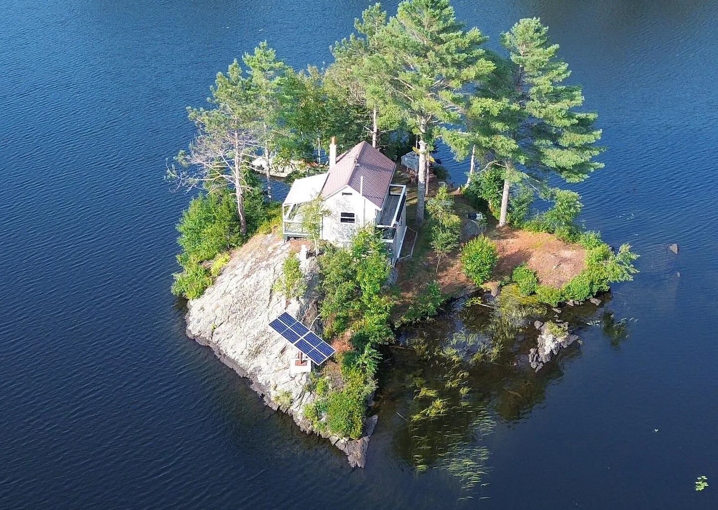 A drone shot of 1 Nay Pond Island, Milan, N.H., featuring a cottage, solar power, and a dock.