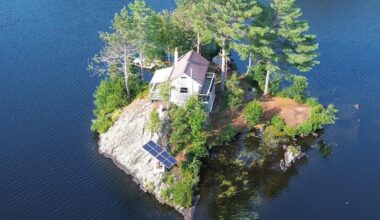 A drone shot of 1 Nay Pond Island, Milan, N.H., featuring a cottage, solar power, and a dock.