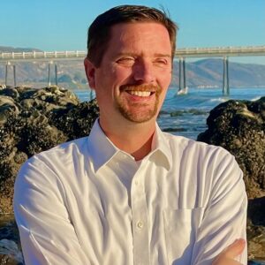 Closeup of Matthew Sutton standing against a rocky shore.