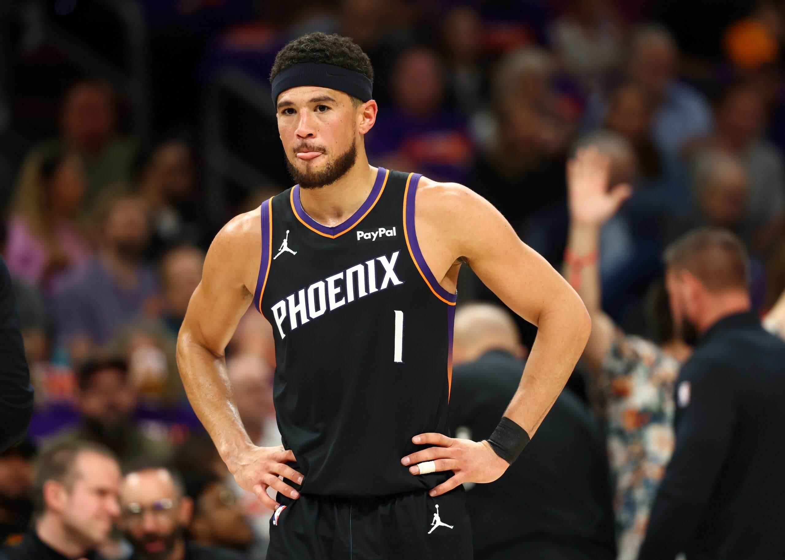 Phoenix Suns guard Devin Booker stands with his hands on his hips and gazes at the court during an NBA game.