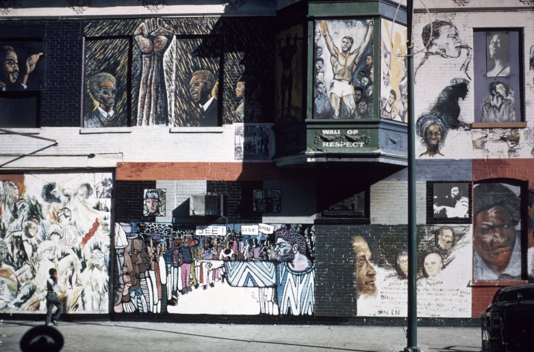 A color photo of the Wall of Respect mural on the side of a two-story brick building in Chicago. The photo shows more than a dozen notable Black figures from different arenas, such as politics and the arts. The mural is painted in sections, by different artists.