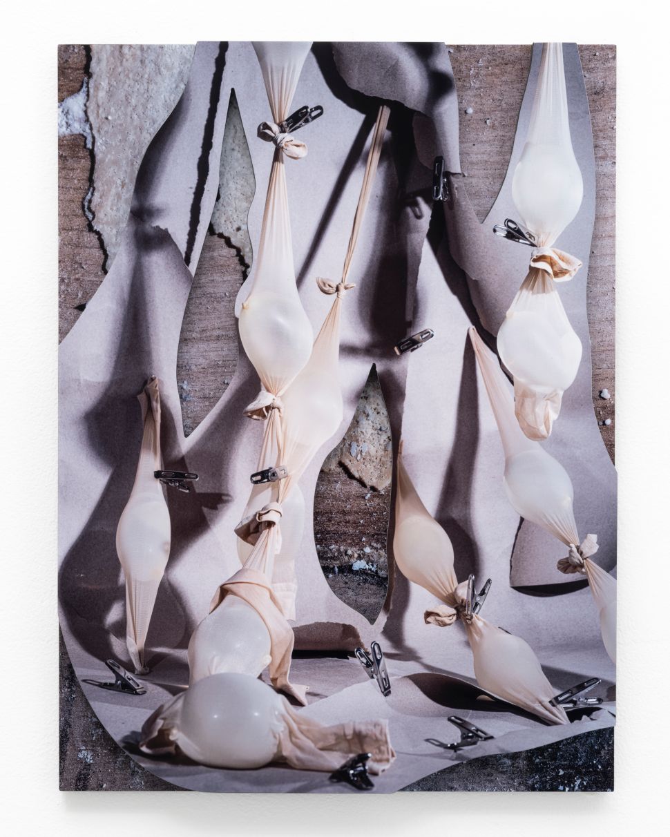 A mixed-media photographic work shows stretched latex forms pinned over a fragmented image of a human body, blending sculpture and photography.