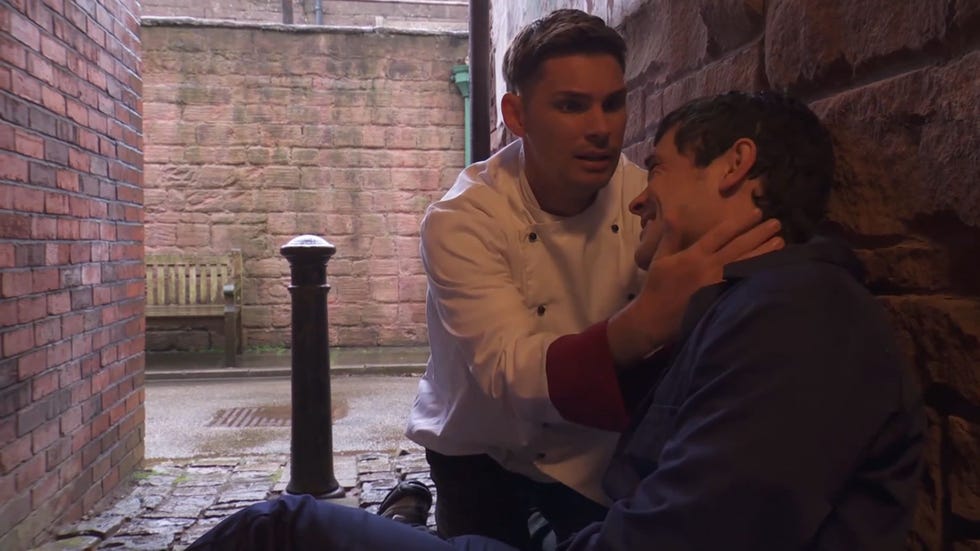 hollyoaks ste hay in his chef whites comforting a sitting down rex gallagher in his blue boiler suit in the alleyway