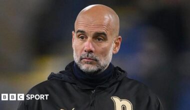 Guardiola in a black jacket with gold details watching on from the sidelines.