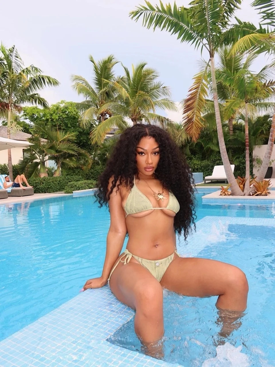 Person sitting at the edge of a swimming pool surrounded by palm trees.