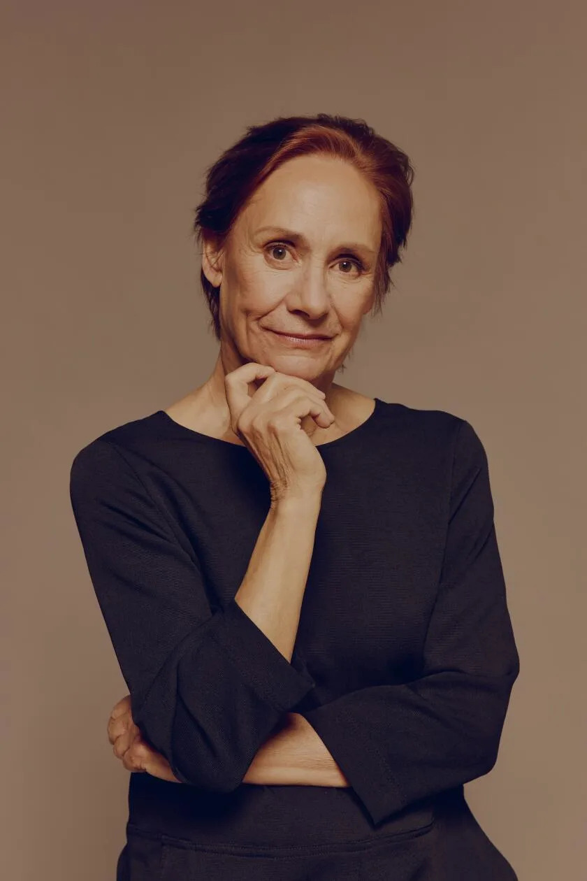 A woman in a black top holds a hand under her chin.