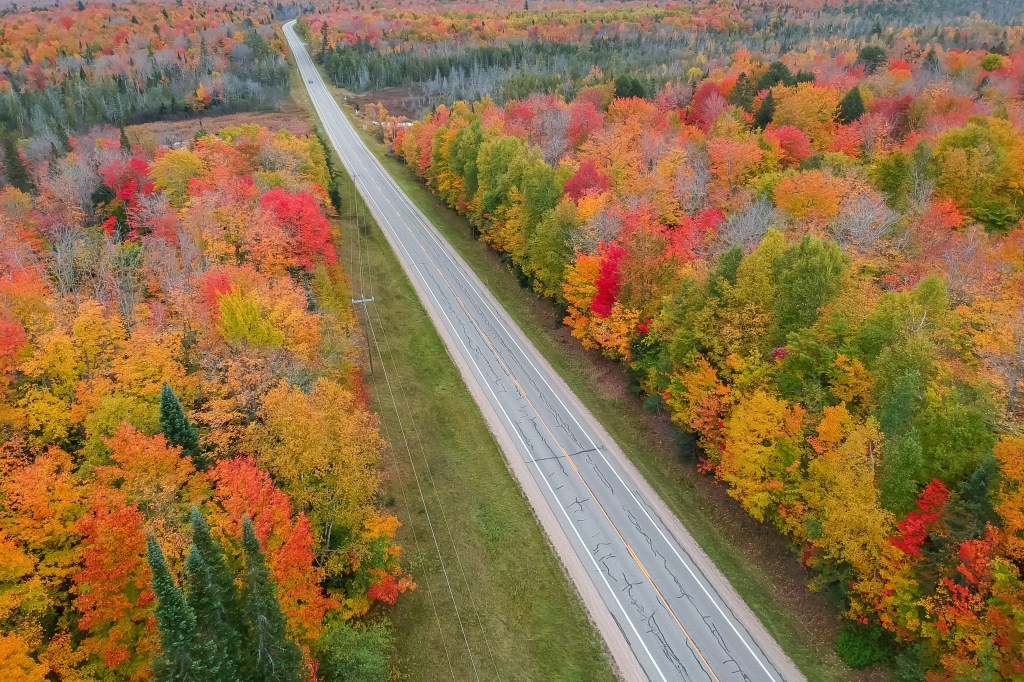 Aerial view of a scenic highway in Michigan's Upper Peninsula surrounded by vibrant fall foliage.