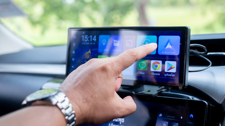 Person's hand touching a car infotainment screen with Apple CarPlay, Android Auto