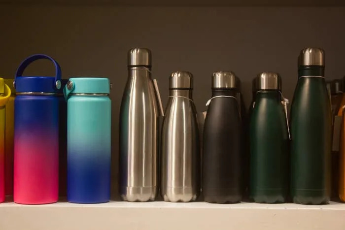 Various reusable water bottles, including metal and insulated styles, are displayed on a shelf, highlighting sustainable lifestyle choices