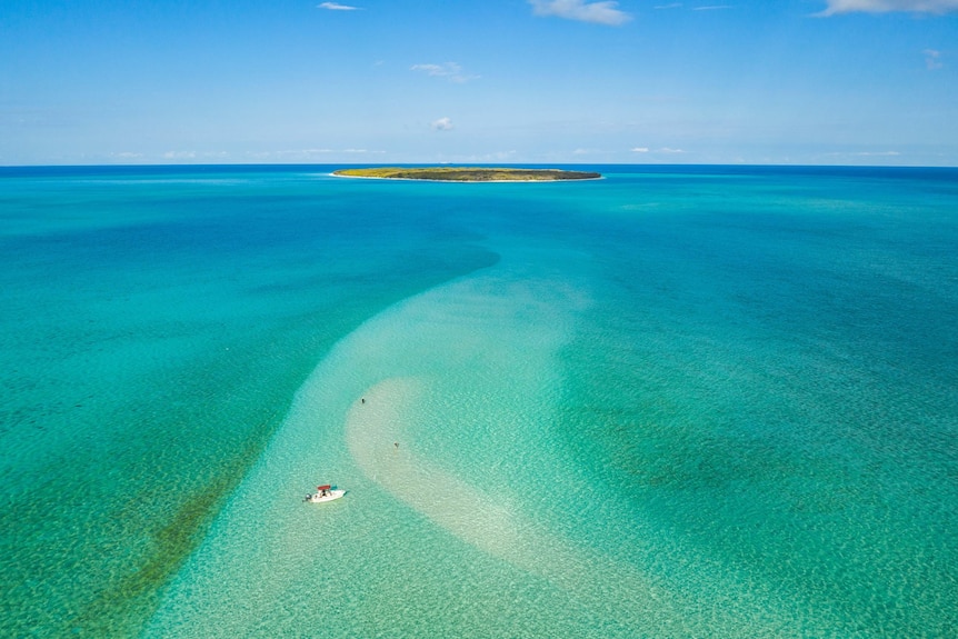 An aerial of a coral cay island with a small boat fishing near the reef