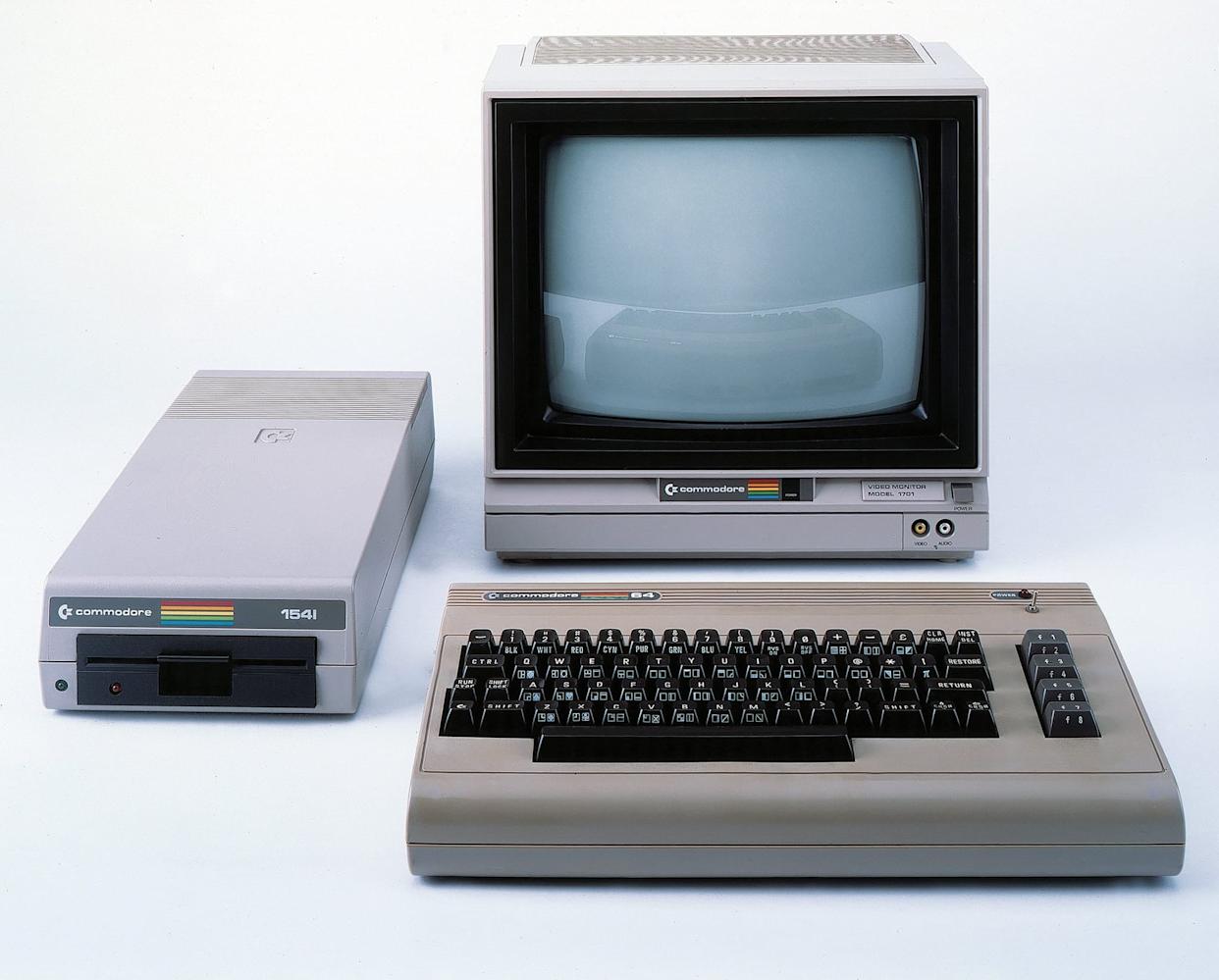 A vintage Commodore 64 computer set with a monitor, keyboard, and 1541 floppy disk drive, all with Commodore branding and rainbow stripes, displayed against a white background.