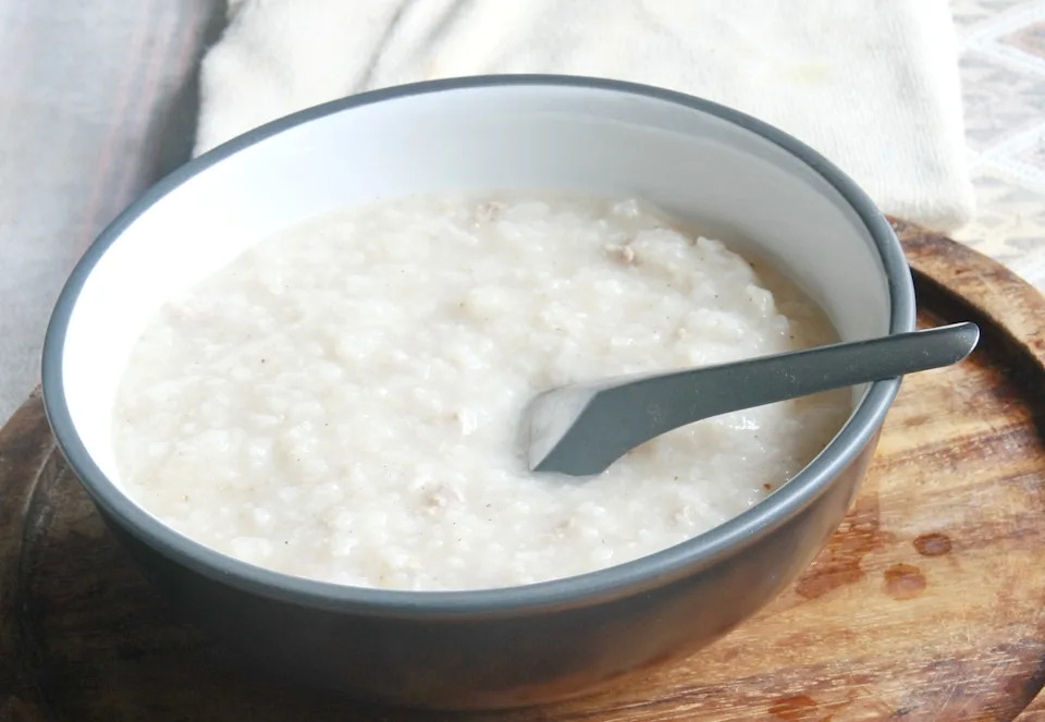A bowl of oatmeal with a spoon on a wooden tray, placed on a patterned fabric