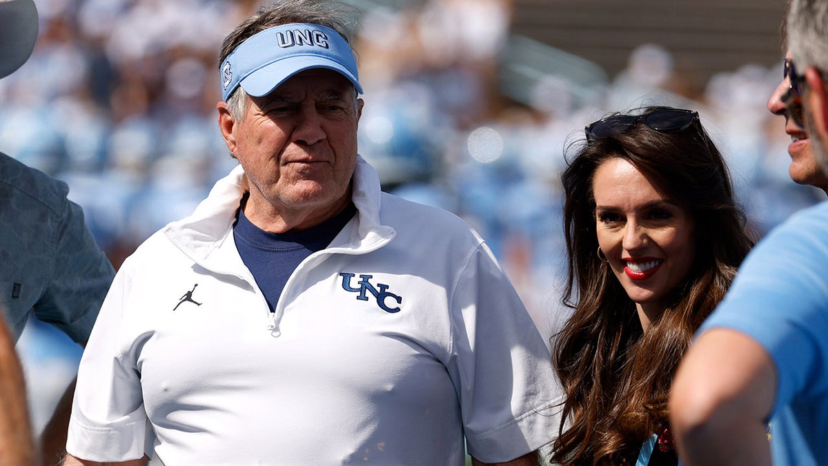 Head coach Bill Belichick and Jordon Hudson standing on the sidelines at Kenan Memorial Stadium