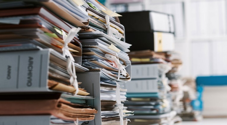 Tall stacks of different paper documents and file folders in an office.