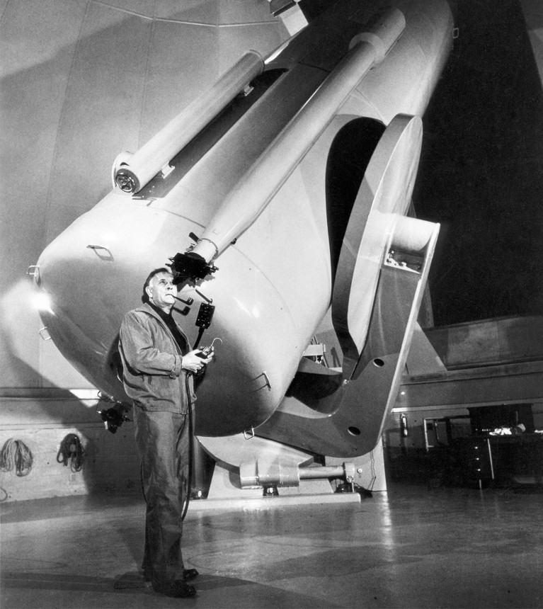 Edwin Hubble operating a large telescope inside an observatory dome.