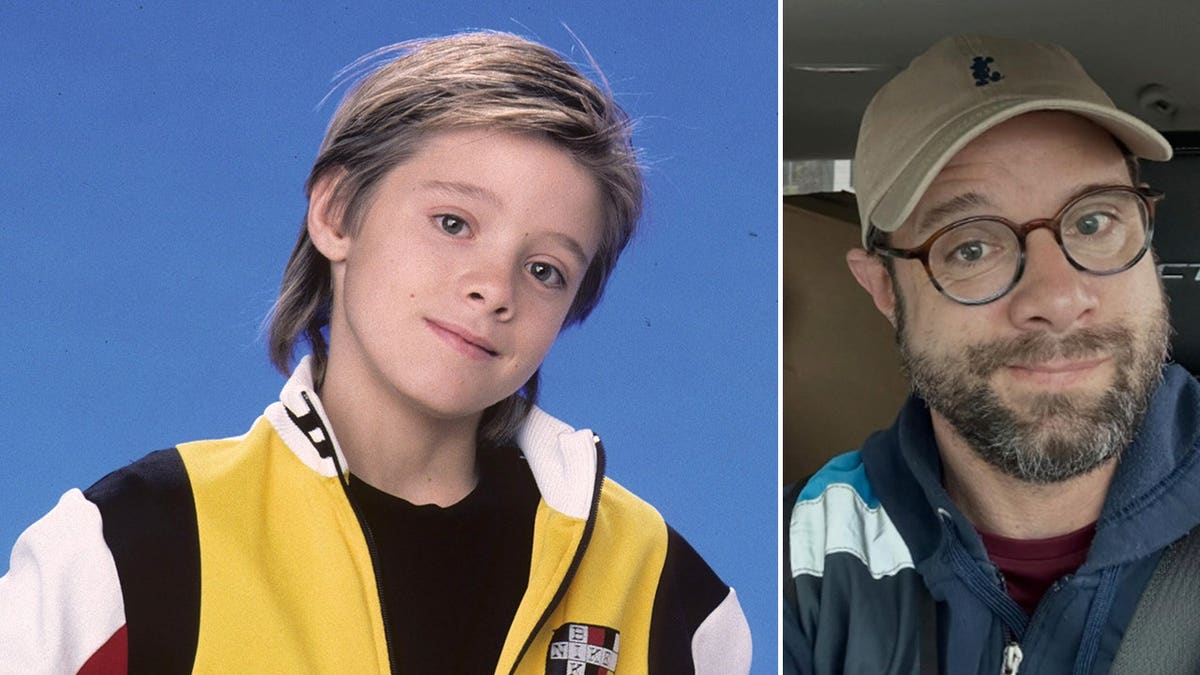 Child star Danny Pintauro, wearing round glasses and a beige baseball cap, sits in the driver’s seat of a car, smiling slightly, with boxes and bags visible in the back seat.
