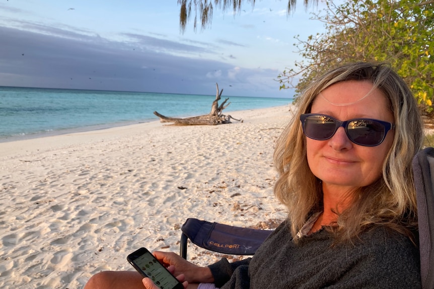 A woman with sunglasses sitting on white sandy beach