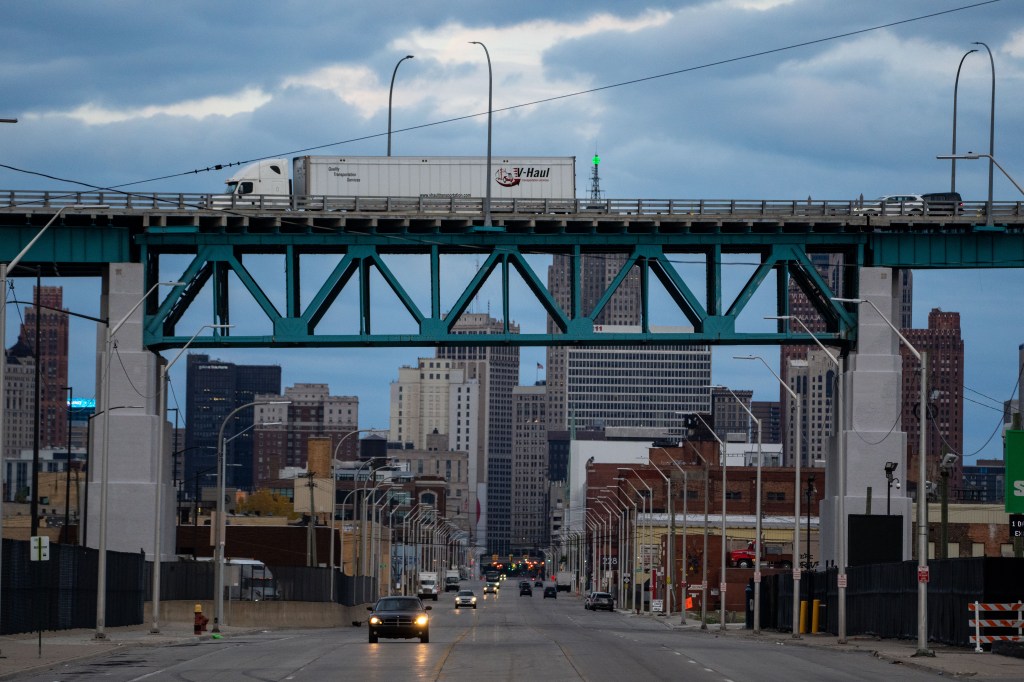 A V-Haul truck crosses the Ambassador Bridge over a street leading into the Detroit skyline.