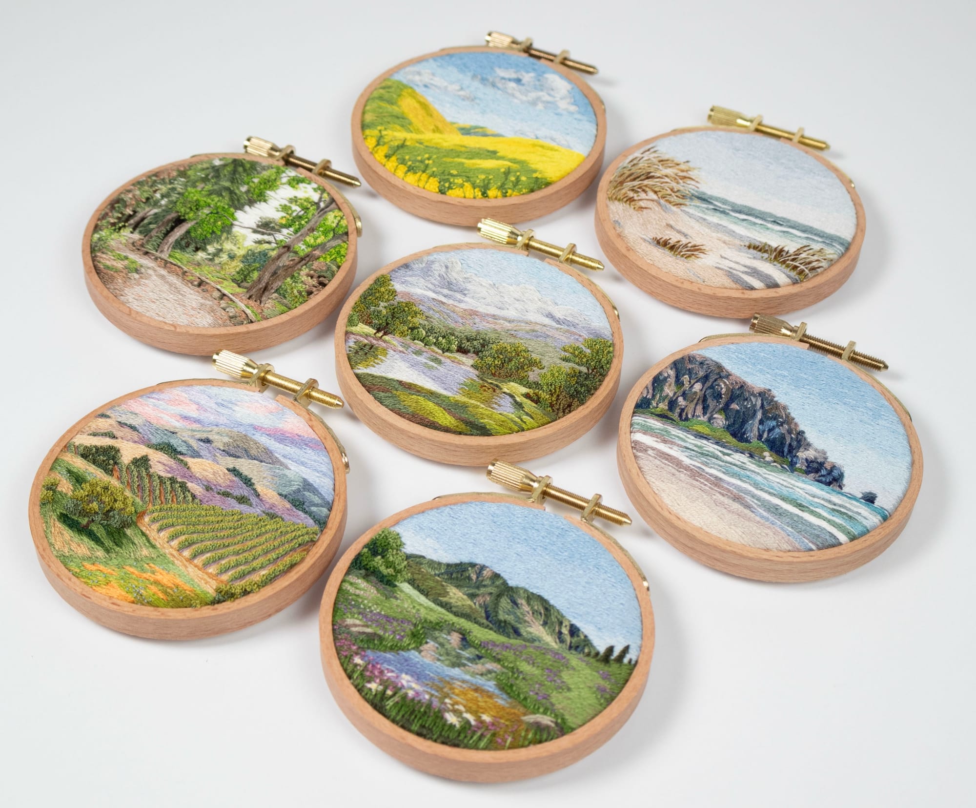 a collection of lush landscape embroideries in light wood hoops by Cassandra Dias