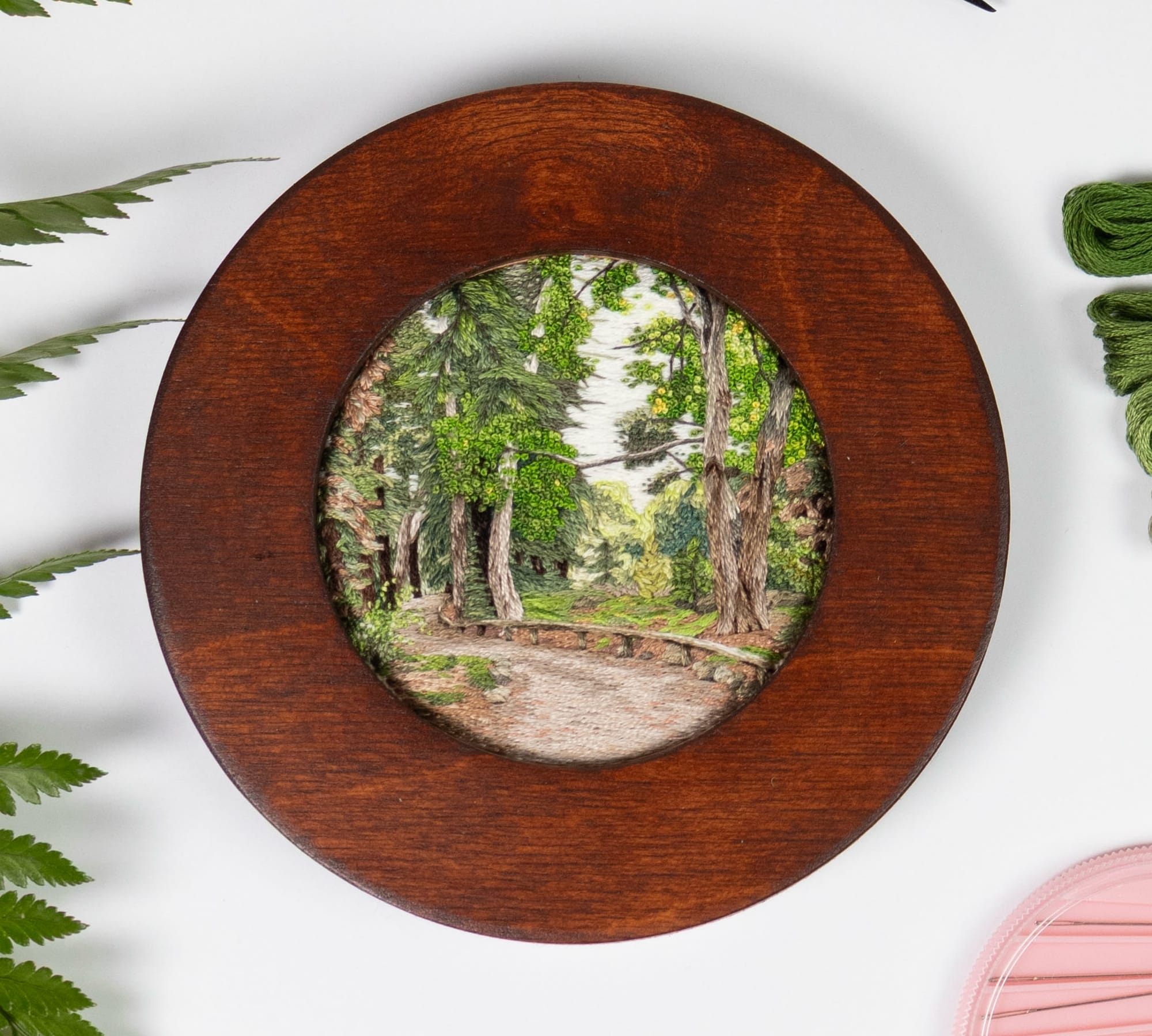 a lush landscape embroidery in a dark wood frame by Cassandra Dias