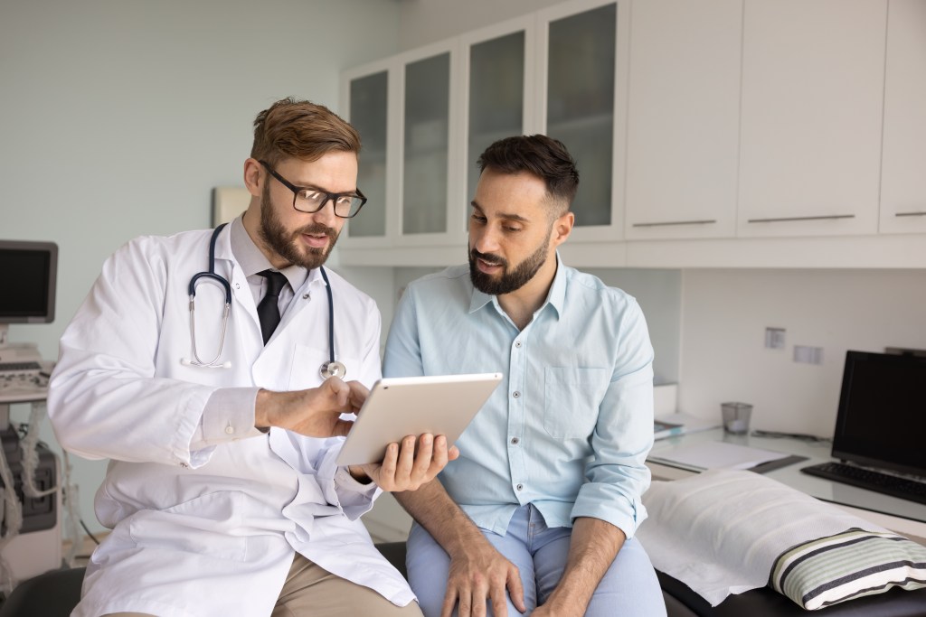 Male doctor discussing therapy plan with a male patient using a tablet.