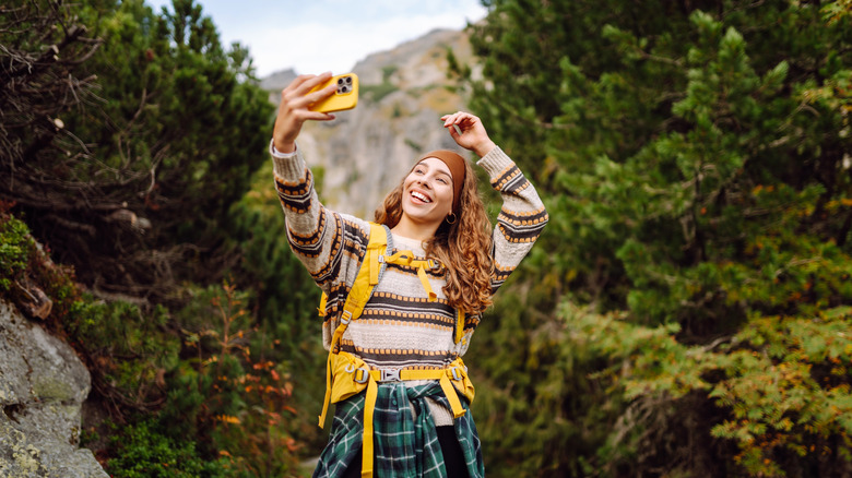 a woman hikes in the woods, using her phone to take a selfie