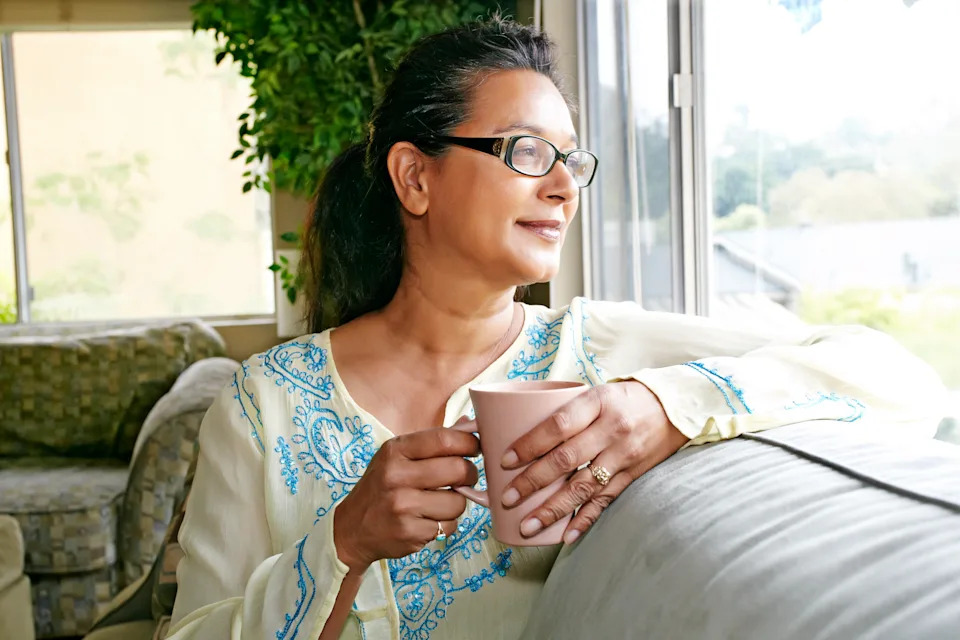 Mixed race woman having cup of coffee on sofa