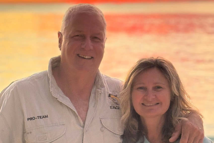 A man holds his arm around a woman with a sunset in the background