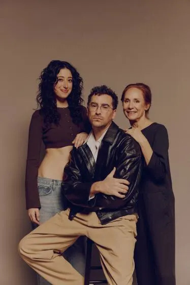 Two women flank a man in a black leather jacket seated on a stool.
