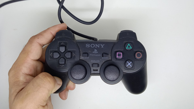 A hand holding a Sony PlayStation wired controller