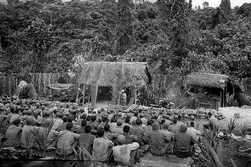 black and white image of American troops sitting on the ground of a training centre in vanuatu with forest surrounding them