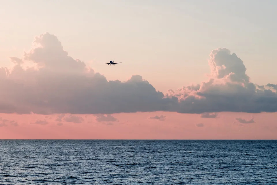 Airplane flying over the ocean with clouds in the backdrop, highlighting travel or business aspects in work and money contexts