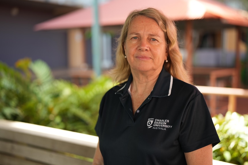 A woman in a blue shirt stands facing the camera