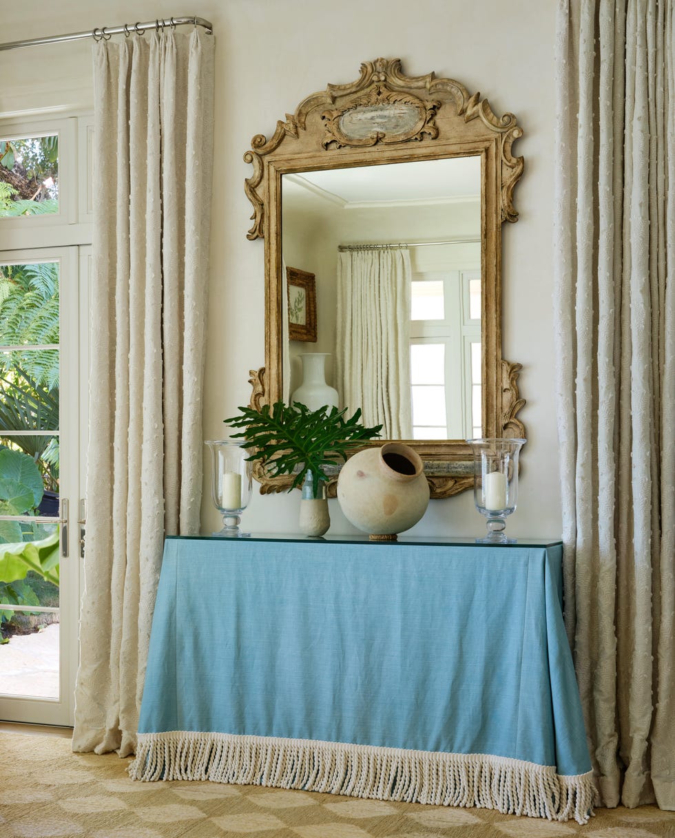 Decorative console table with a mirror above, featuring plants and vases.