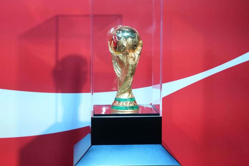 The FIFA World Cup trophy displayed in a glass case against a red and white background.