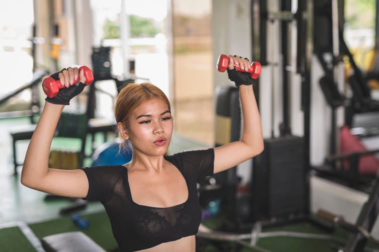 A woman performs a seated dumbbell press in the gym.