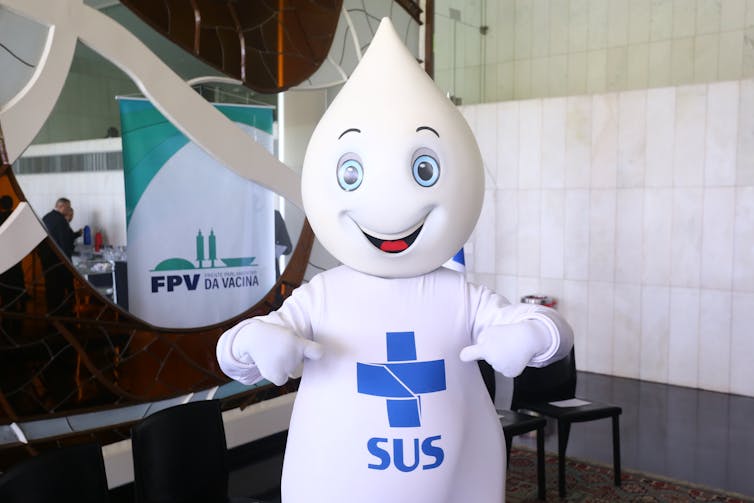 A white vaccine droplet with a smiling face and the logo of Brazil's public health system on its belly.