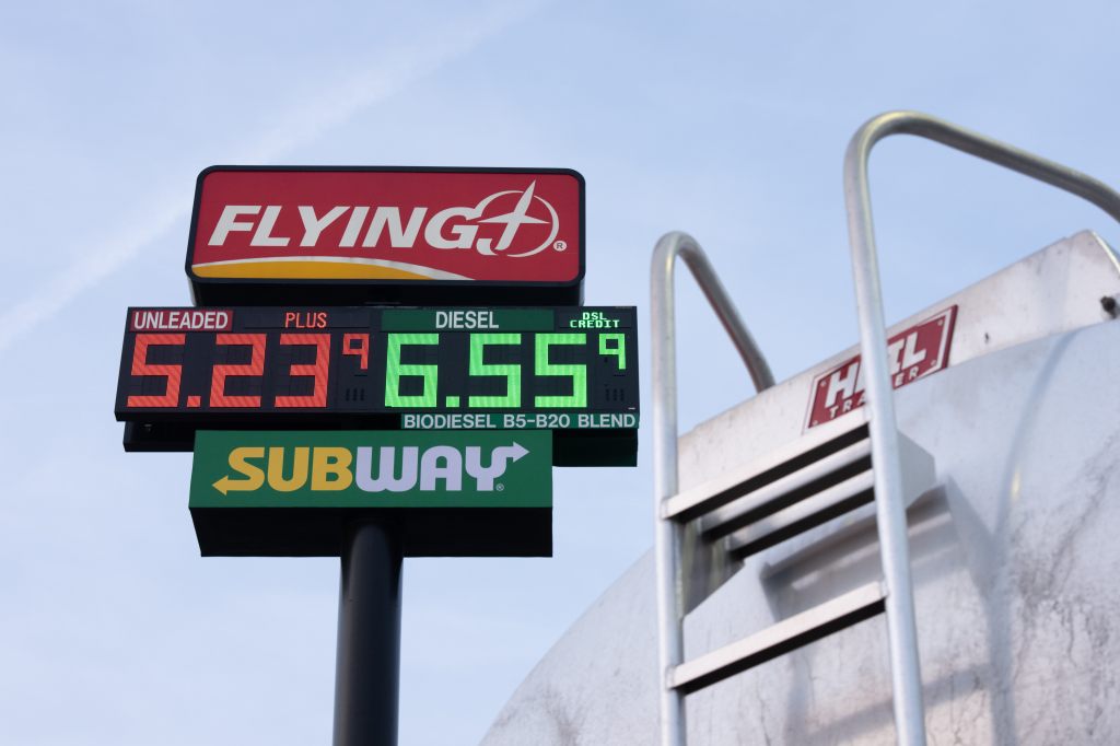 Gas prices displayed on a sign as 5.23 for unleaded and 6.55 for diesel, with a fuel transport truck in the background.