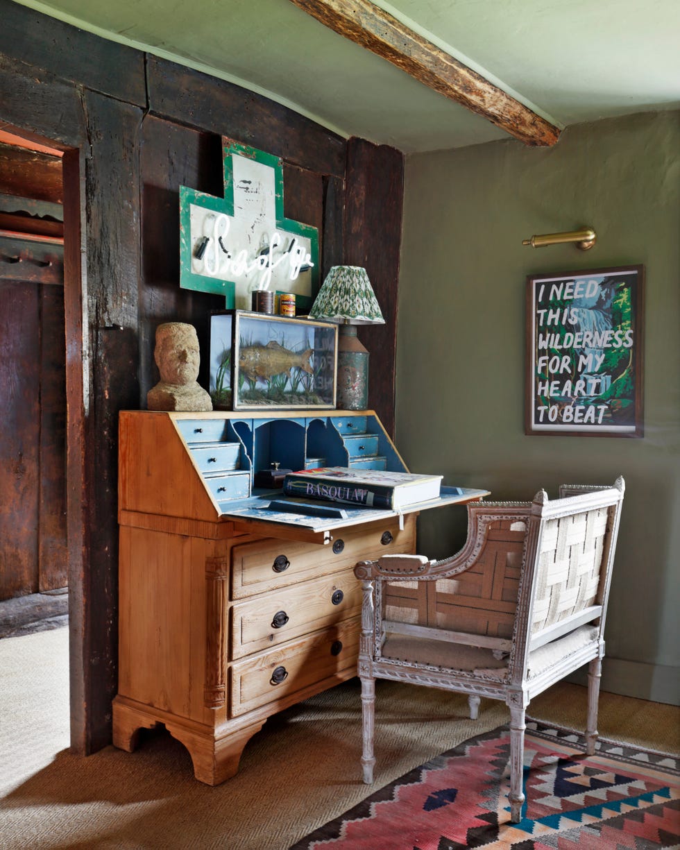 wooden secretary with a chair in front of it and pieces of art above it on the wall
