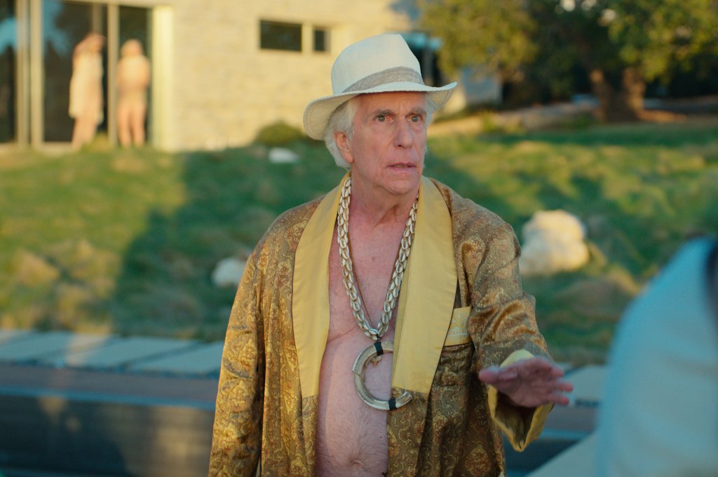 Henry Winkler in "Loot" wearing a hat, robe, and shell necklaces.
