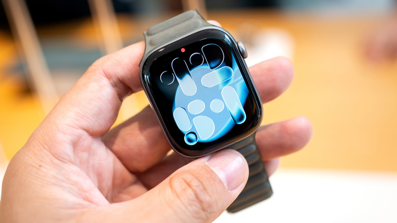 Close-up of a hand holding an Apple Watch Series 11 with a gray silicon band