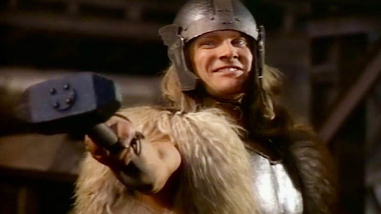 Thor holds out his hammer while smiling