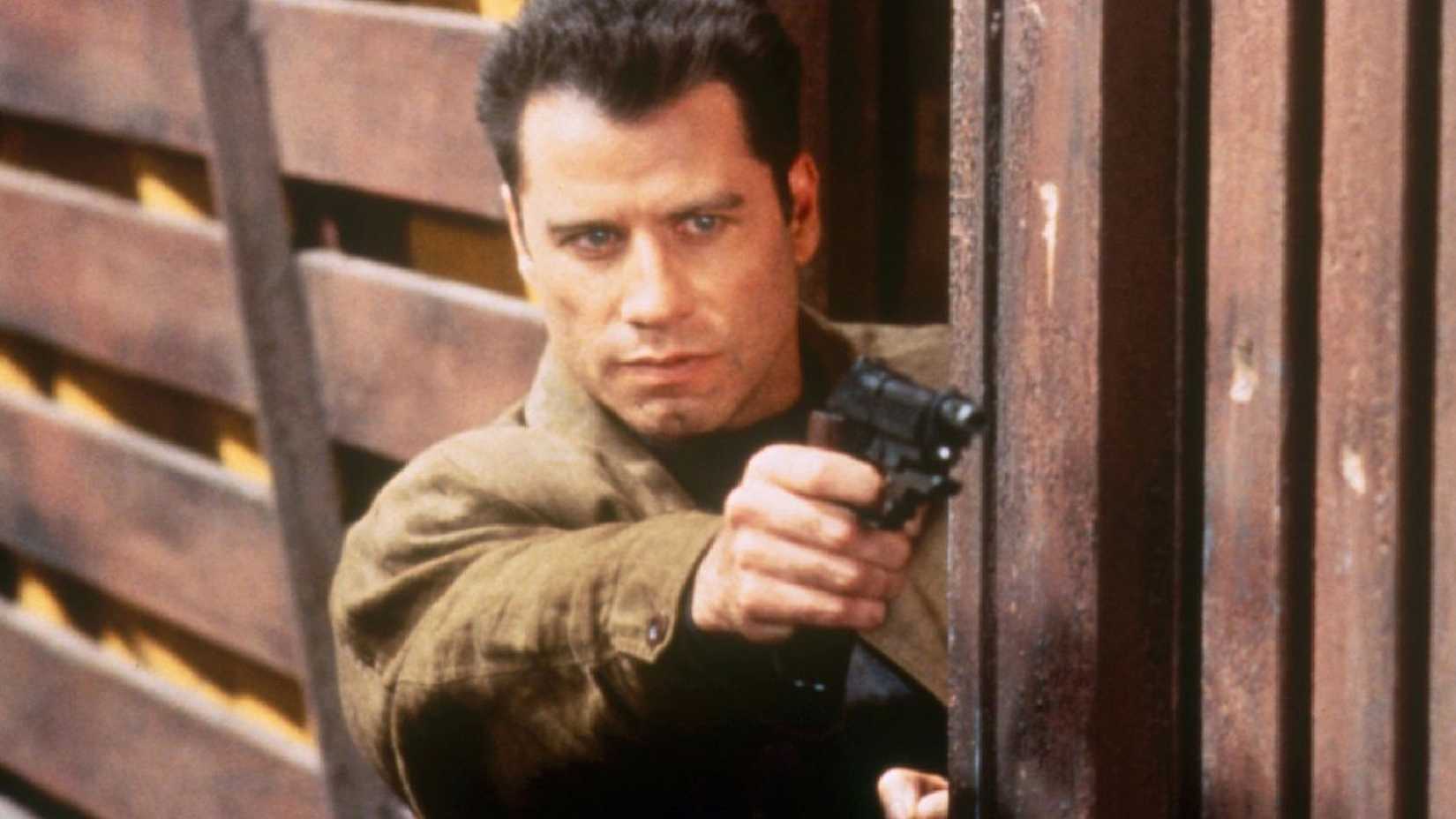 John Travolta as Deakens hanging out of a train car holding a pistol in Broken Arrow