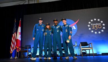 The four Artemis II crew members stand side-by-side and smiling in their blue flight suits on a stage at NASA Johnson. Bel