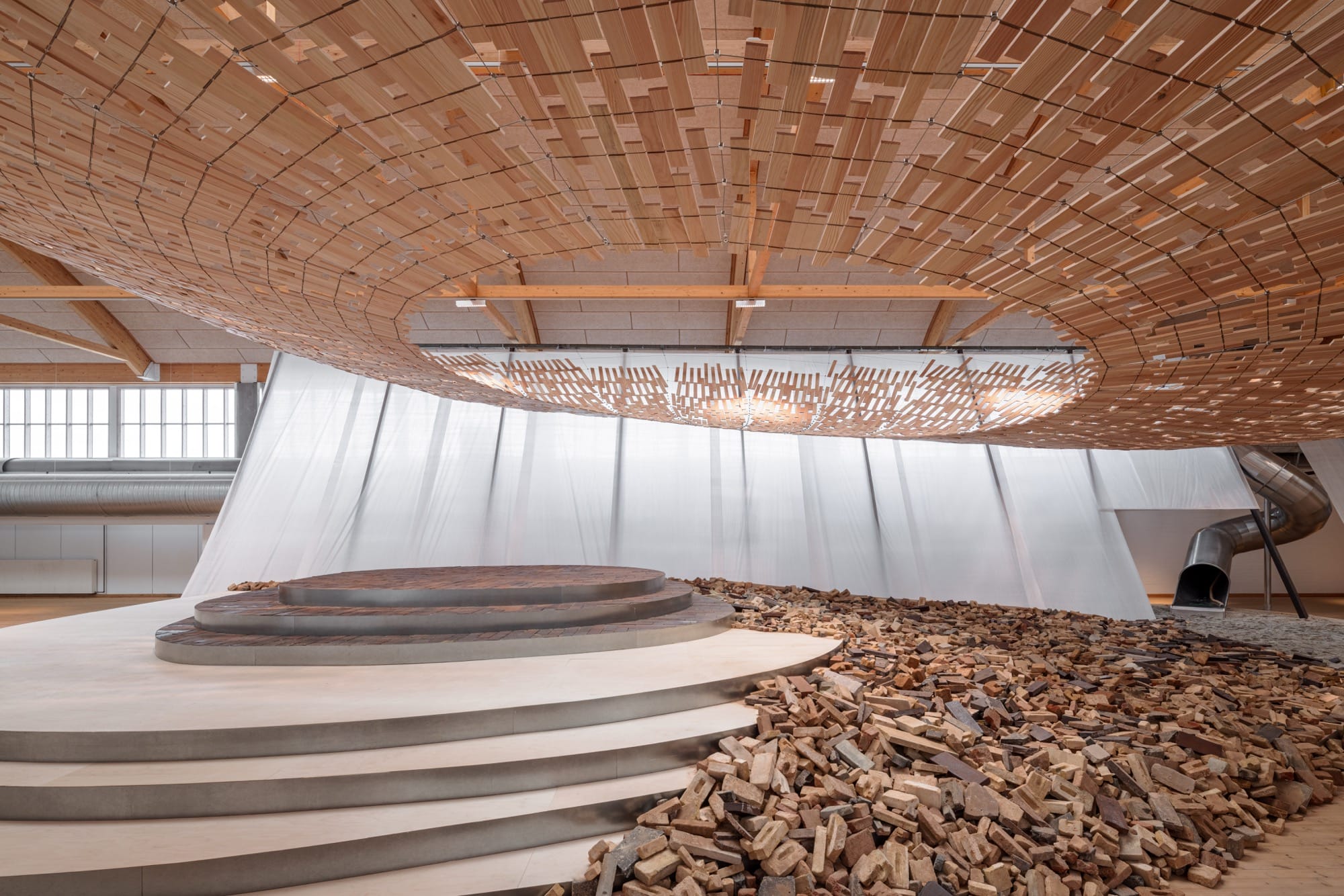 light streams through a wooden canopy in a large scale installation of wood and brick by Kengo Kuma