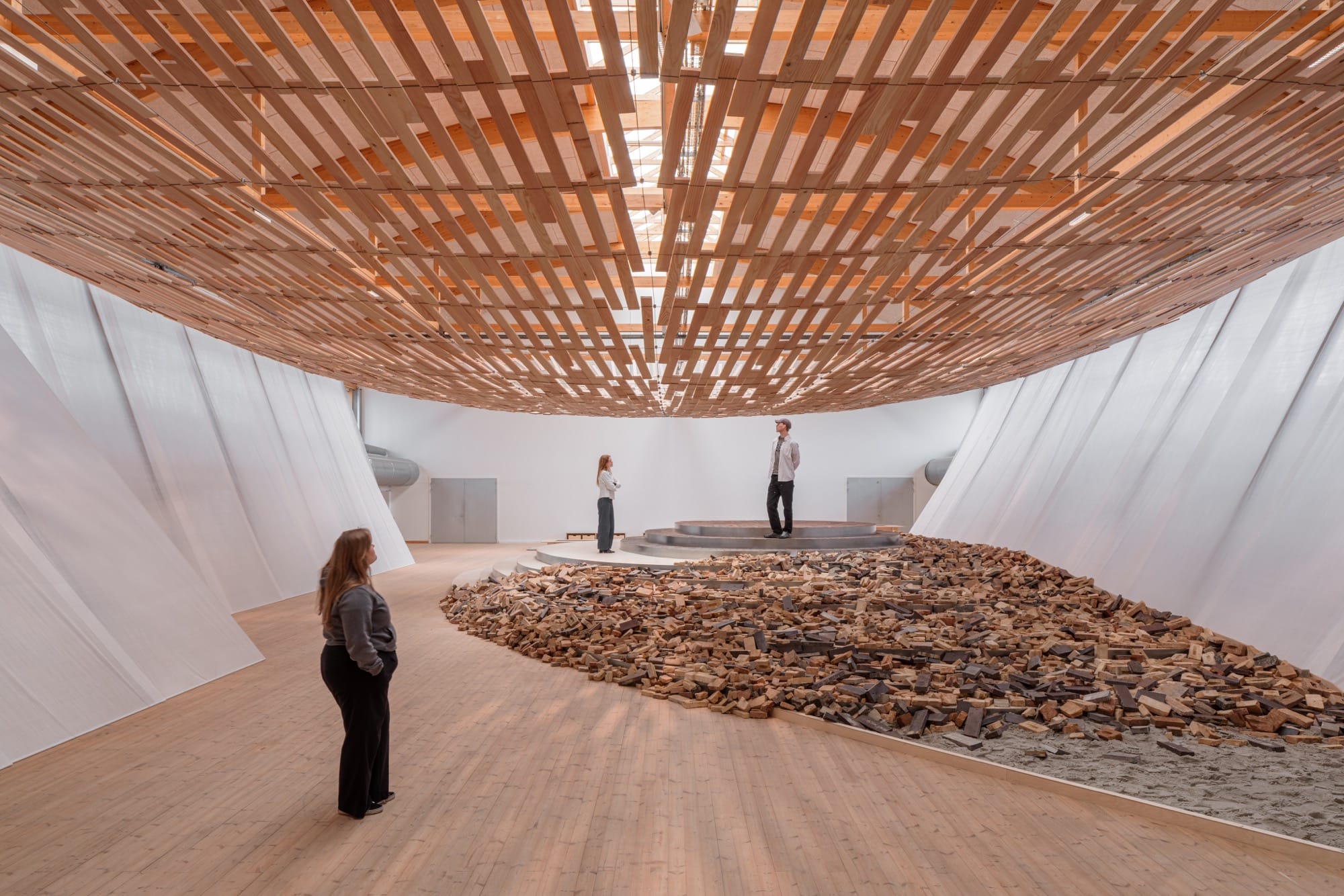 visitors enjoy an installation in which light streams through a wooden canopy by Kengo Kuma