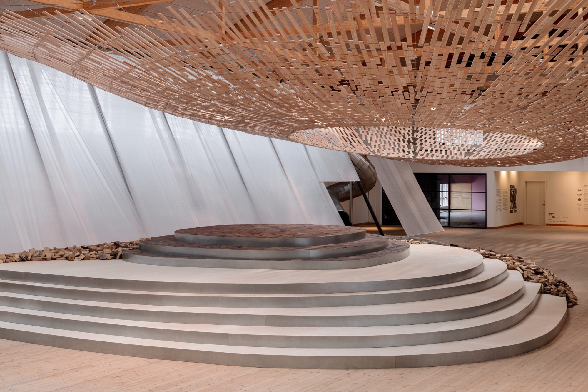 light streams through a wooden canopy in a large scale installation of wood and brick by Kengo Kuma